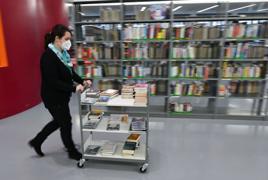 Una empleada traslada libros a los estantes de una biblioteca.