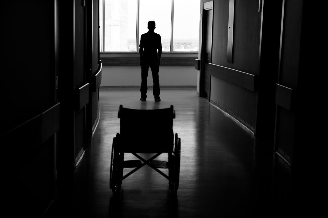 Un hombre observa la ventana tras dejar atrás una silla de ruedas. 