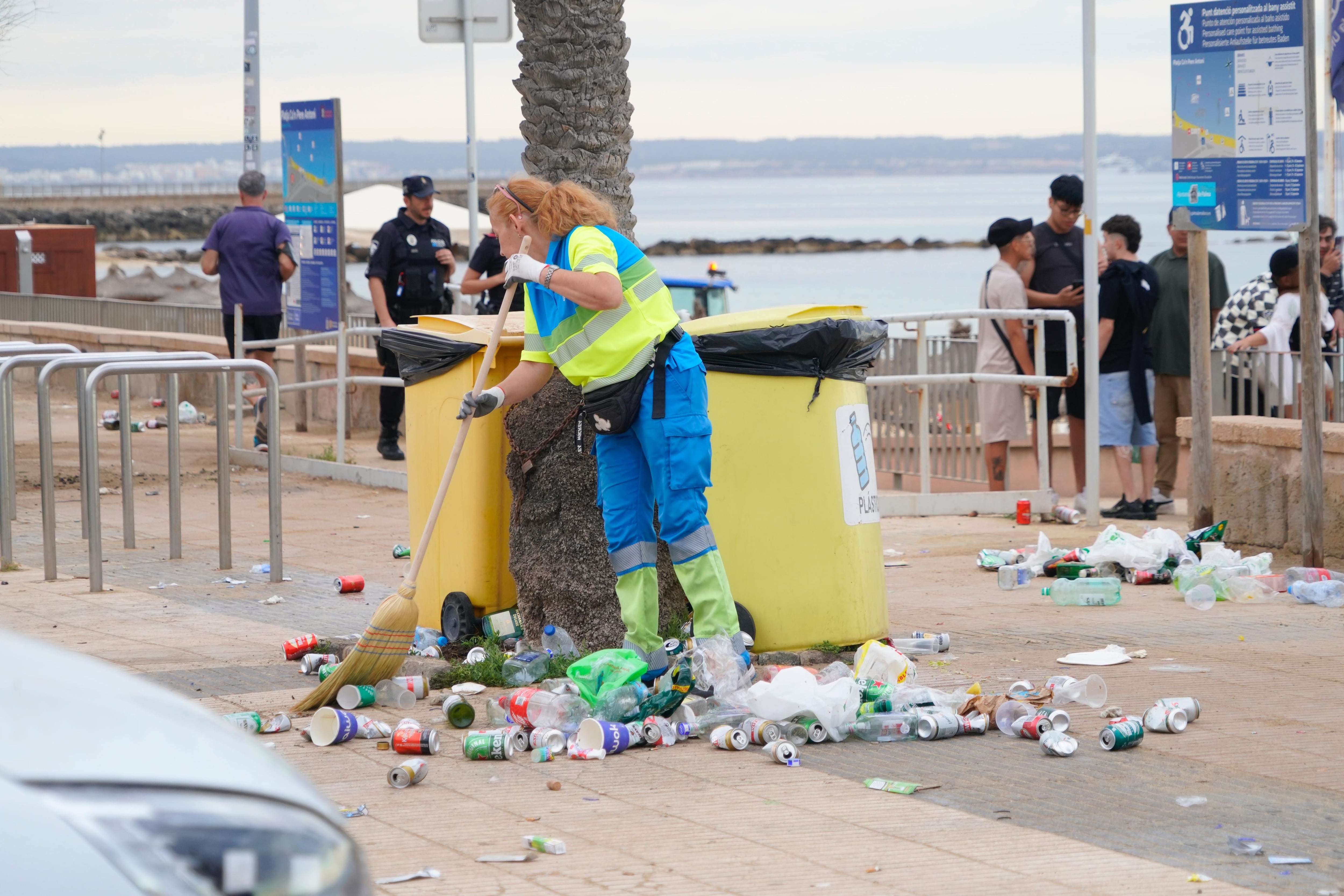 Una trabajadora de Emaya recogiendo residuos en el suelo, junto a unos contenedores, en el paseo junto a la playa, tras la noche de San Juan. - AYTO. DE PALMA