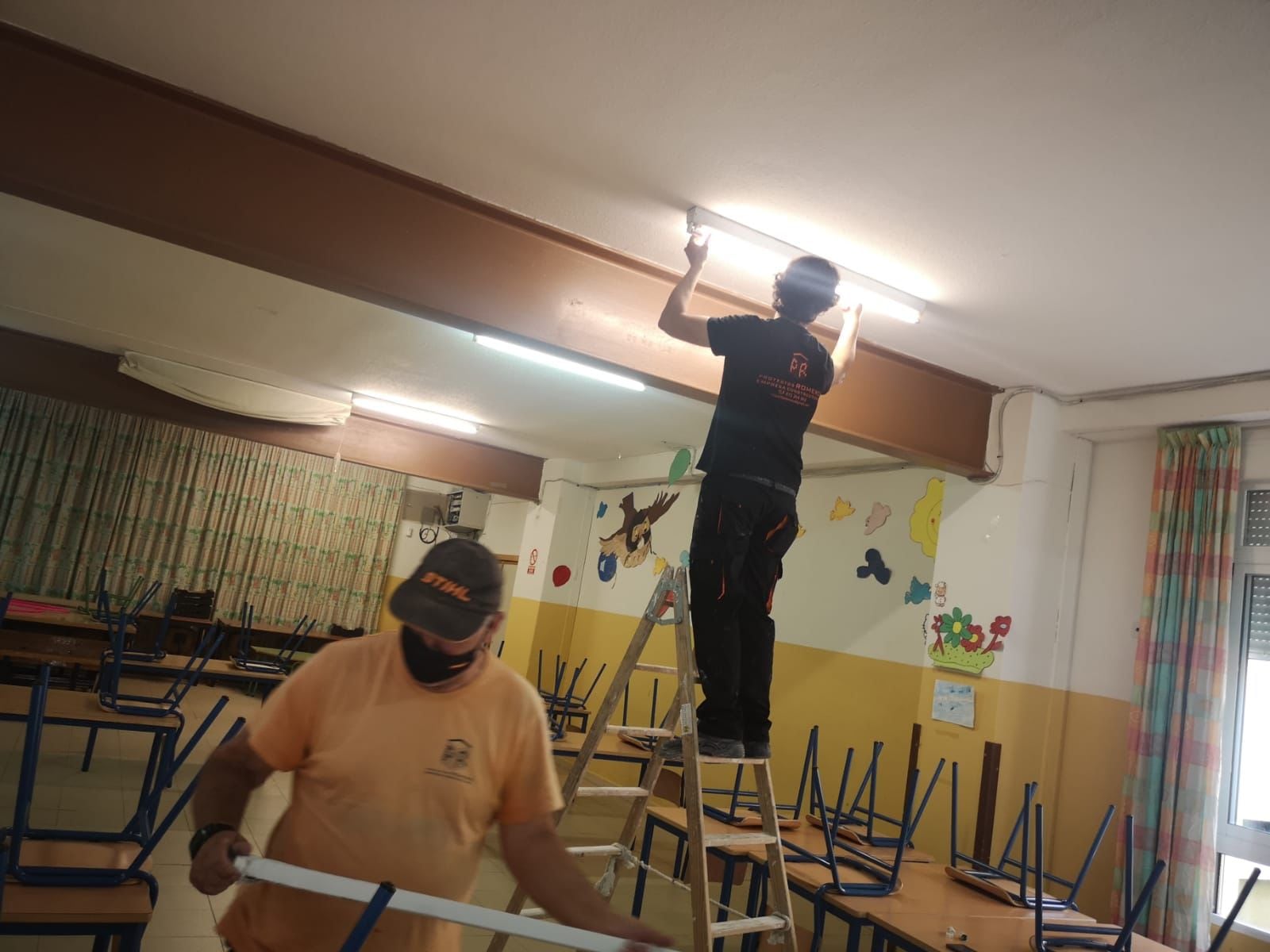 Dos operarios cambian las luminarias de una clase en un colegio de la capital.