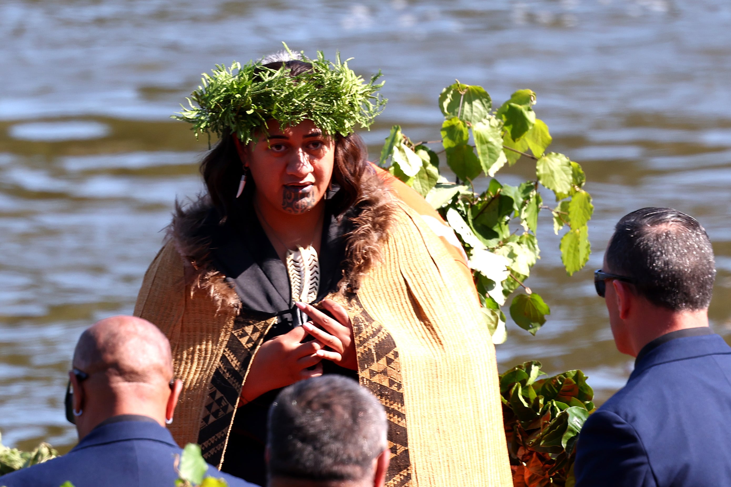 La reina maorí  Nga wai hono i te po,  arropada por una capa, con una corona de plantas sobre la cabeza y con un collar tallado en forma de hoja en el pecho.