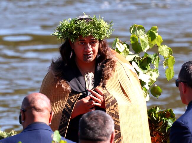 La reina maorí Nga wai hono i te po, arropada por una capa, con una corona de plantas sobre la cabeza y con un collar tallado en forma de hoja en el pecho.