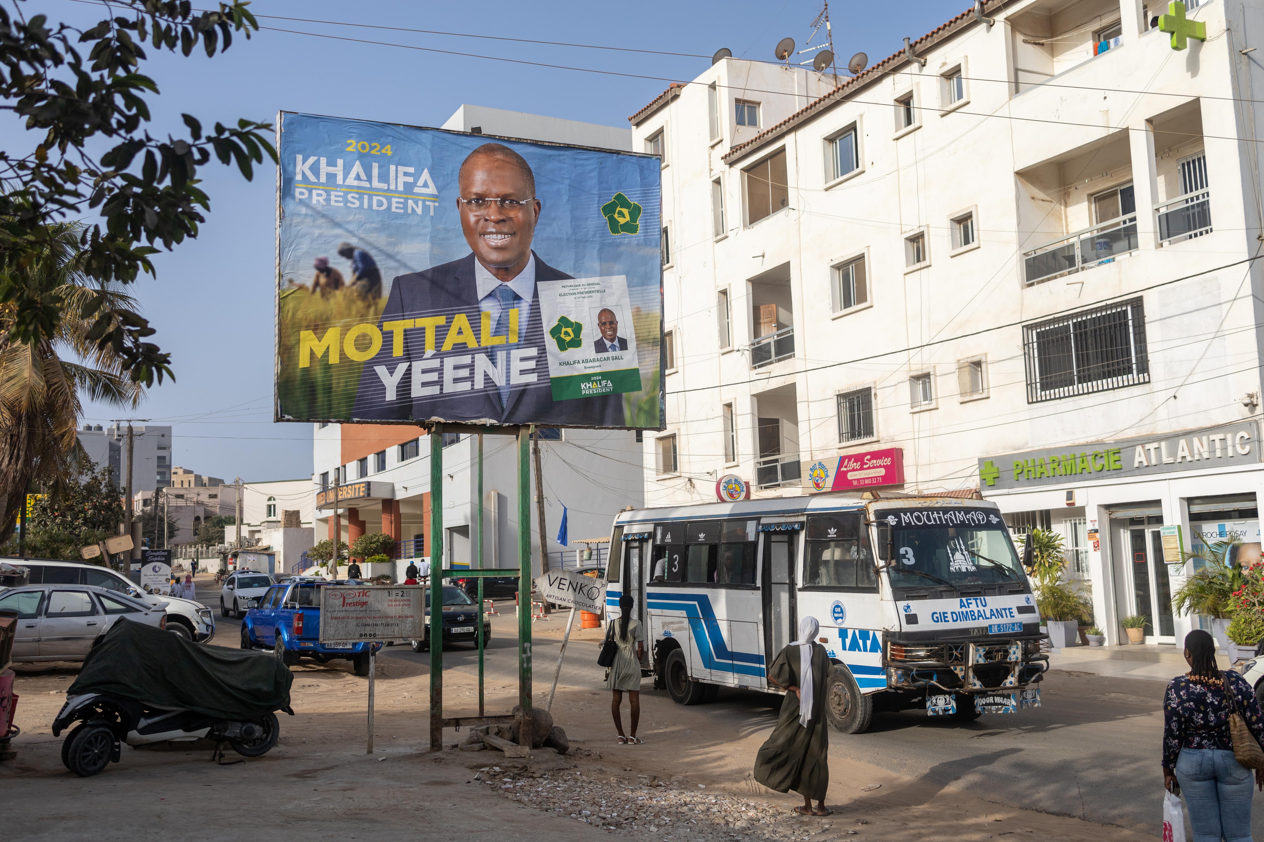 En Dakar, peatones caminan bajo un cartel del opositor Manko Taxawu que opta a la presidencia del gobierno en las elecciones de hoy domingo.