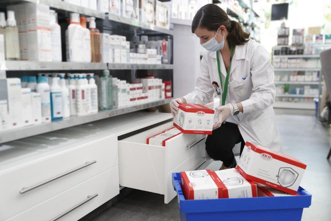 Una farmacéutica coloca cajas con mascarillas.