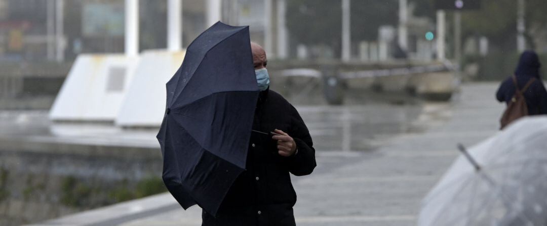 Un hombre con un paraguas camina por el paseo marítimo mientras llueve, a 8 de diciembre de 2021, en A Coruña