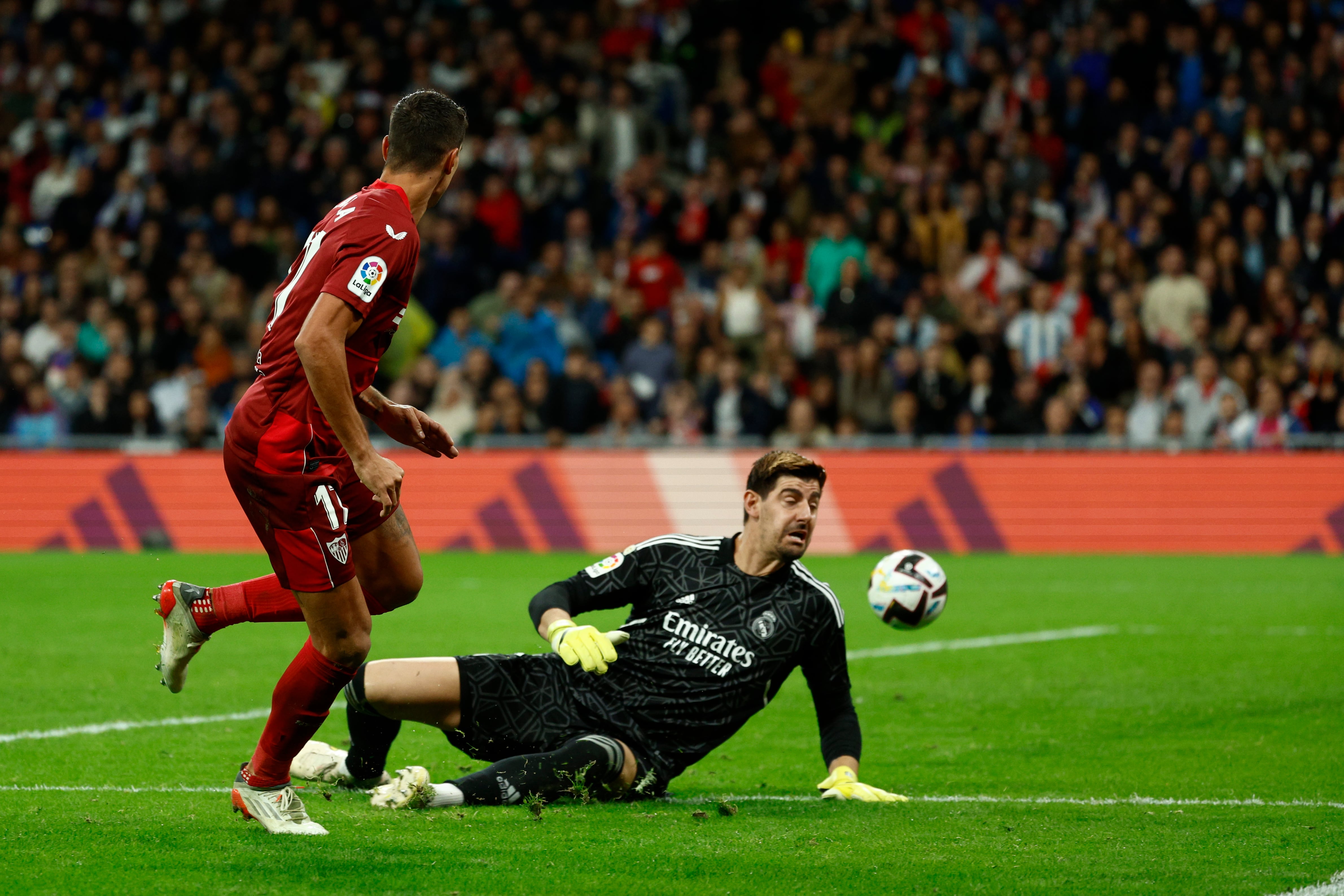 MADRID, 22/10/2022.- El delantero argentino del Sevilla, Erik Lamela (i), intenta superar el guardameta belga del Real Madrid, Thibaut Courtois, para conseguir el primer gol del equipo sevillista durante el encuentro correspondiente a la jornada 11 de primera división que disputan hoy sábado en el estadio Santiago Bernabéu, en Madrid. EFE / Rodrigo Jiménez.

