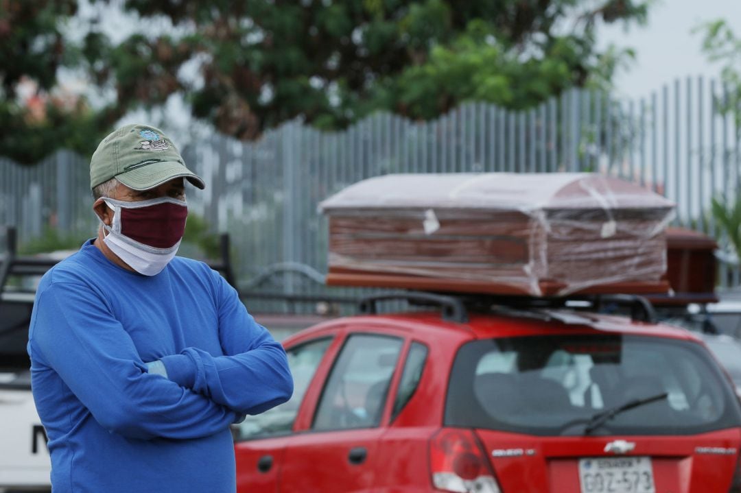 El paciente de una víctima de coronavrus viste una máscara mientras permanece de pie junto a un coche que carga un atáud, en Guayaquil (Ecuador).