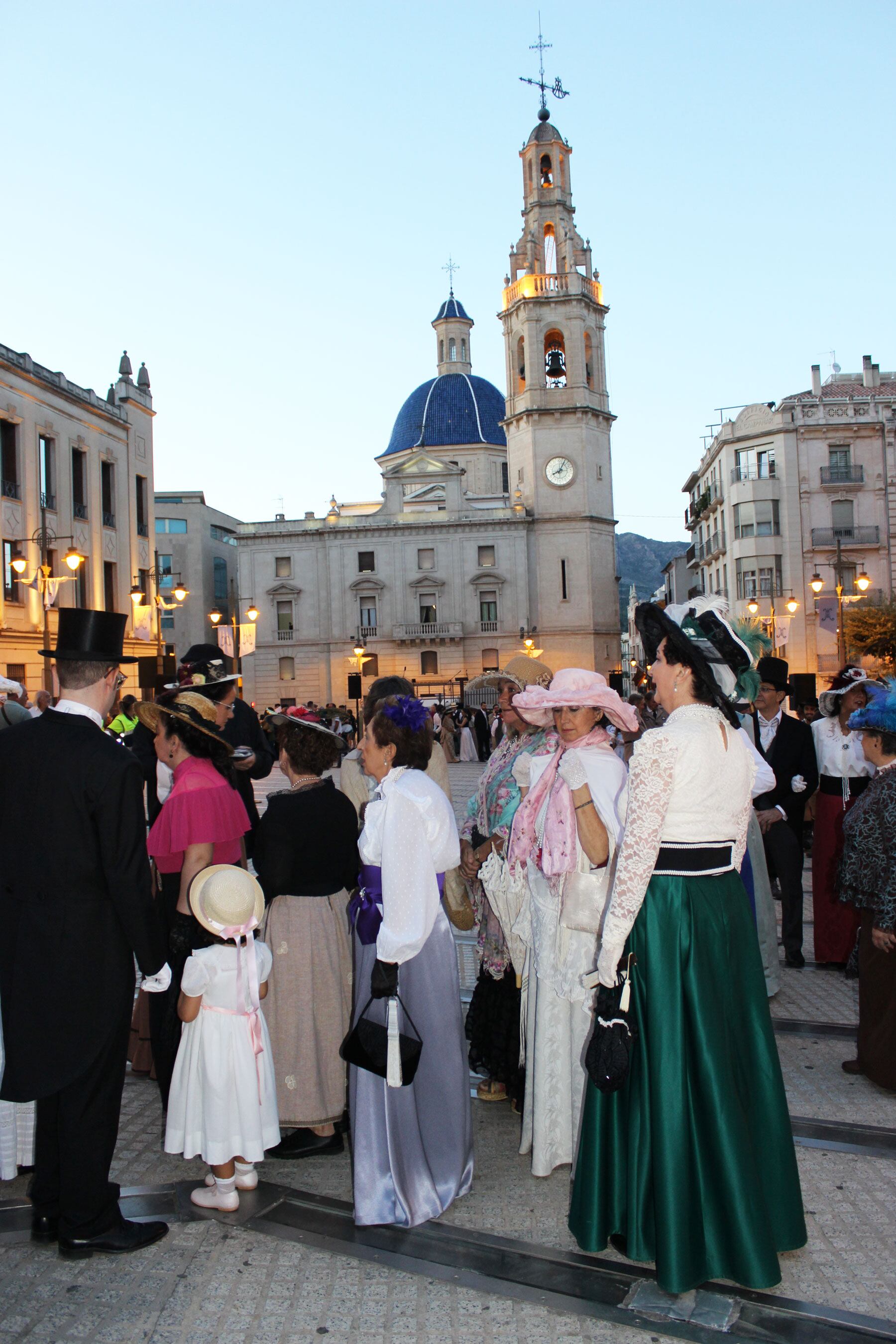 Imagen de participantes en el desfile vestidos de época modernista con el campanario y Santa María al fondo