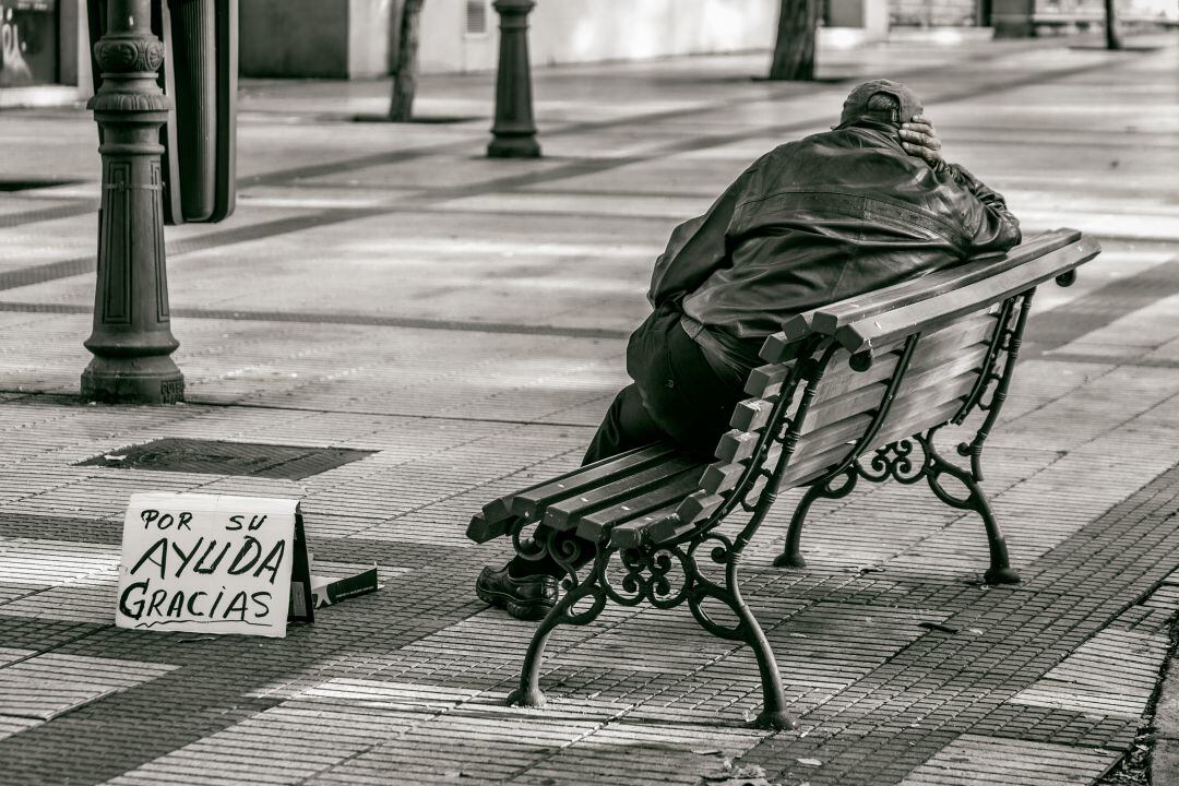 Un hombre pide en la calle con un cartel &quot;por su ayuda, gracias&quot;. 