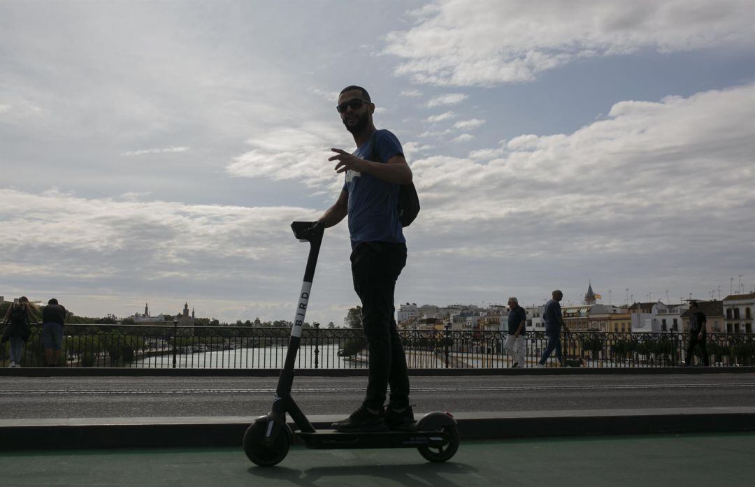 Un joven atraviesa el Puente de Triana con patinete eléctrico