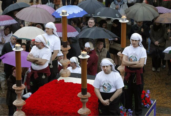 Varios costaleros permanecen en pie junto al paso de la imagen del Cristo de la Misericordia, tras suspenderse la procesión a causa de la lluvia en Oviedo