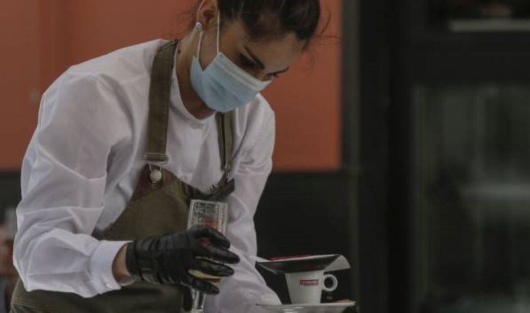 Una camarera con mascarilla y guantes atiende un bar