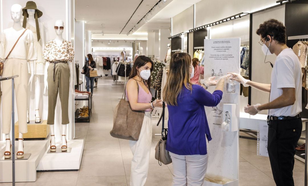 Dos clientas se desinfectan las manos con gel hidroalcohólico a la entrada de una tienda de ropa.