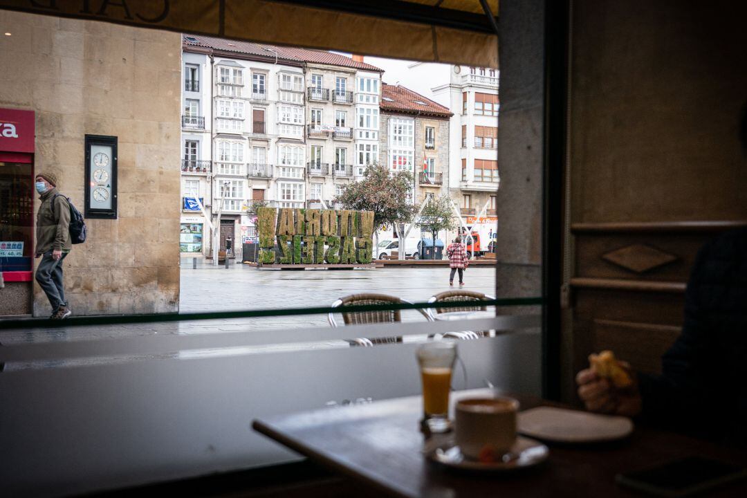 Un comensal desayuna en una cafetería cercana a la plaza de la Virgen Blanca, en Vitoria-Gasteiz, mientras un viandante pasa con mascarilla. Imagen de archivo