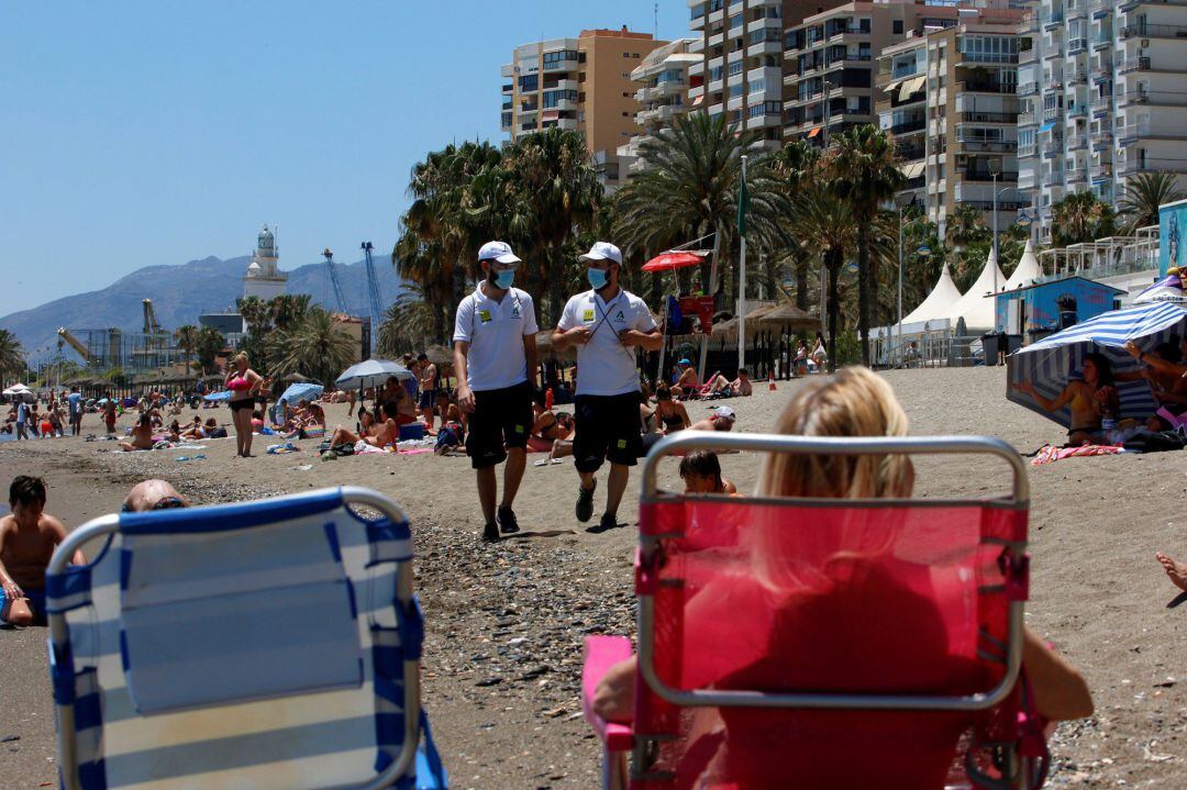 Una pareja de Vigilantes de la playa de Andalucía asesoran a bañistas sobre las medidas preventivas sobre el COVID-19 en la playa de La Malagueta