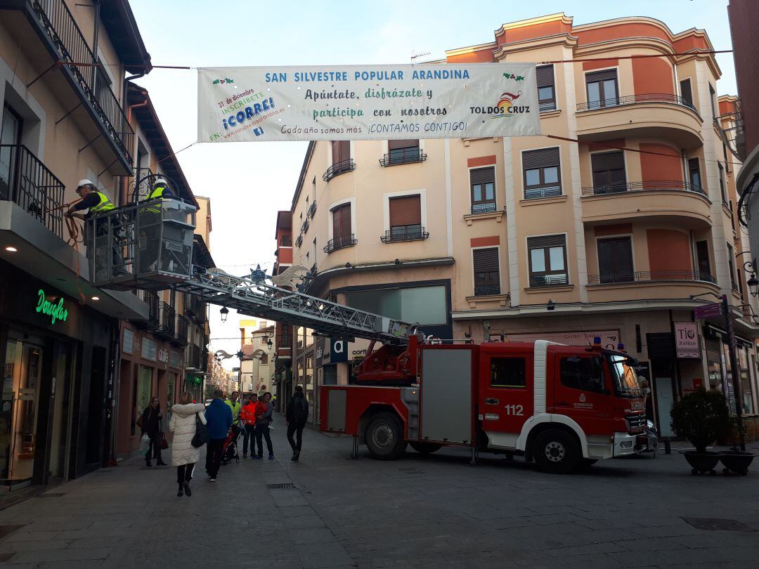 Los miembros de la Asociación Deportiva Bomberos de Aranda de Duero colocan una de las pancartas del recorrido.