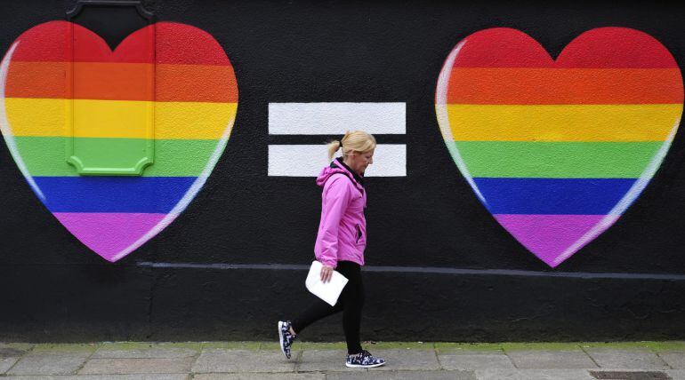 Una mujer camina junto a una pintada de dos corazones con los colores del arcoíris en Dublín, Irlanda.