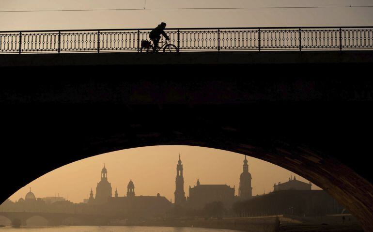 Un ciclista cruza un puente en una gran ciudad europa, la alemana Dresde.