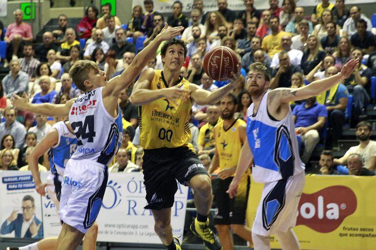 El base de Iberostar Tenerife, Rodrigo San Miguel (c), entra a canasta ante los jugadores del Rio Natura Monbus, Fran Cárdenas (i) y Alberto Corbacho, durante el encuentro correspondiente a la segunda jornada de la liga regular ACB, que han disputado esta