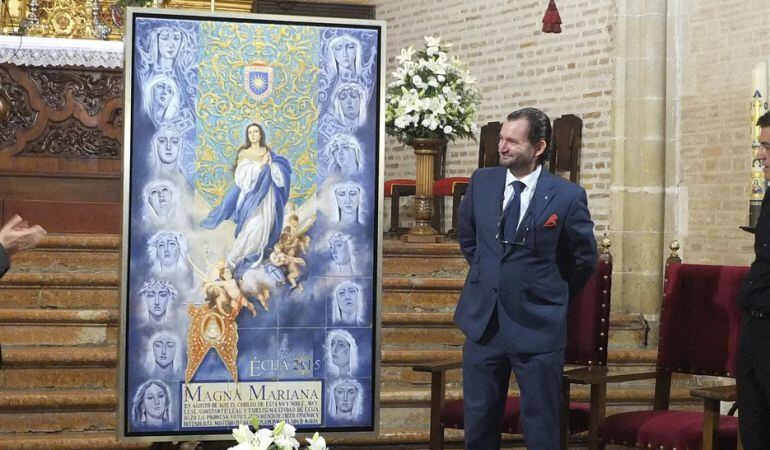 El pintor César Ramírez a la derecha del cartel que realizó para anunciar la Magna Mariana de Écija del próximo 11 de octubre