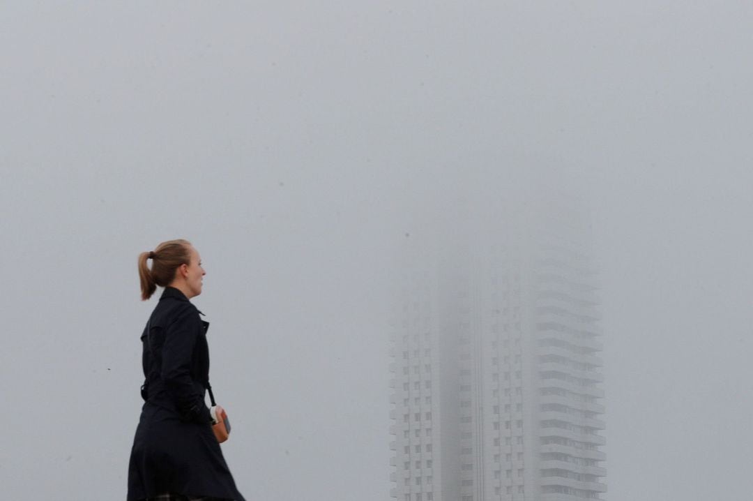 Una persona pasa junto a un edificio envuelto en niebla cuando la Autoridad Portuaria de Valencia.