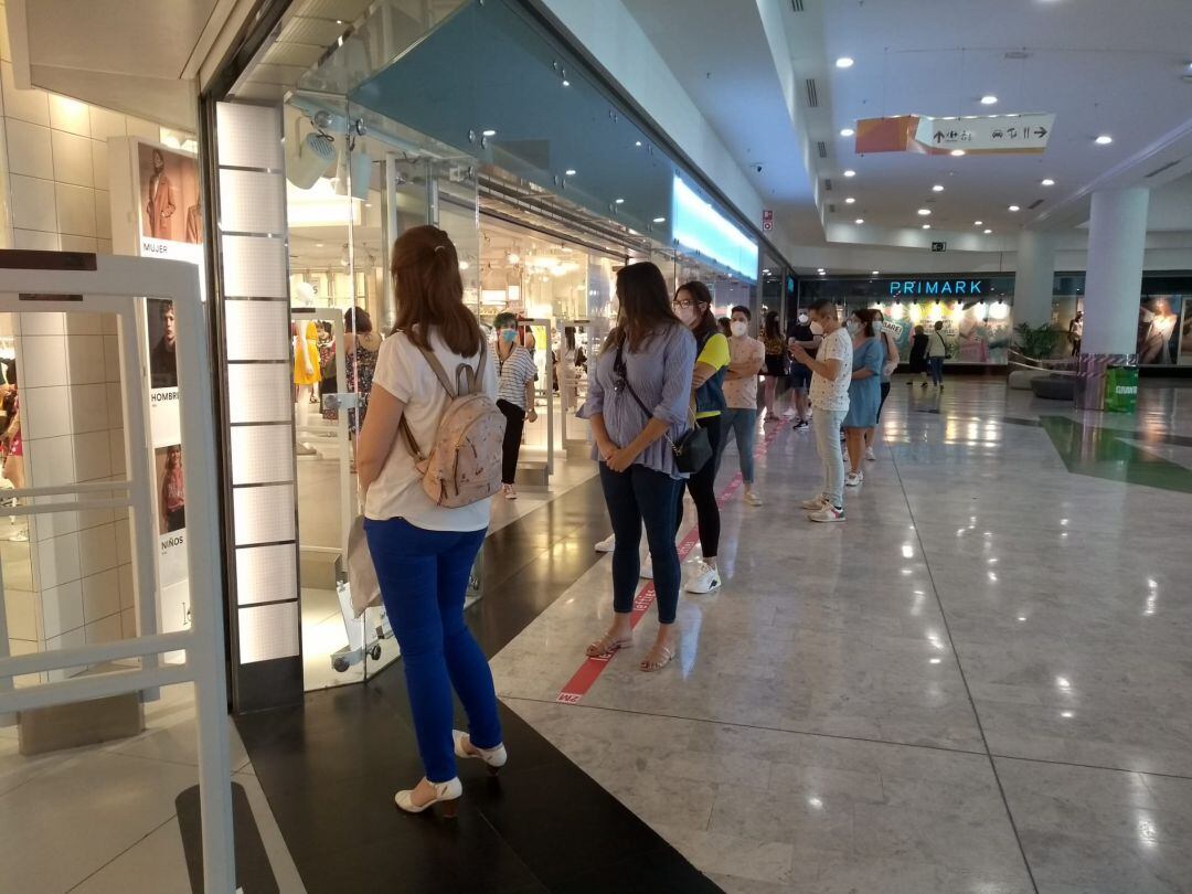 Varias personas guardan fila esperando la entrada a una marca de ropa en el centro comercial Gran Vía.