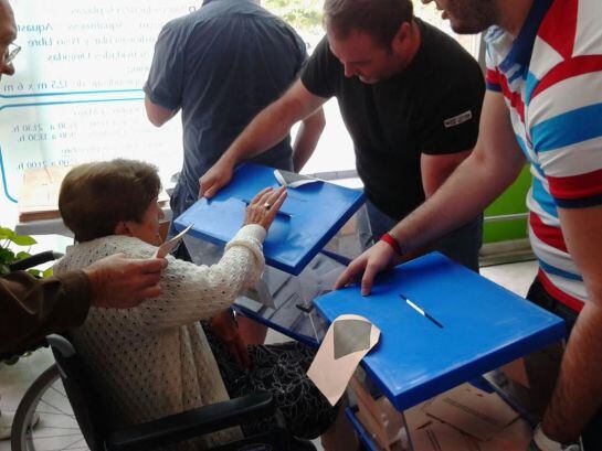 Los componentes de una mesa electoral acercan las urnas a una mujer en silla de ruedas.