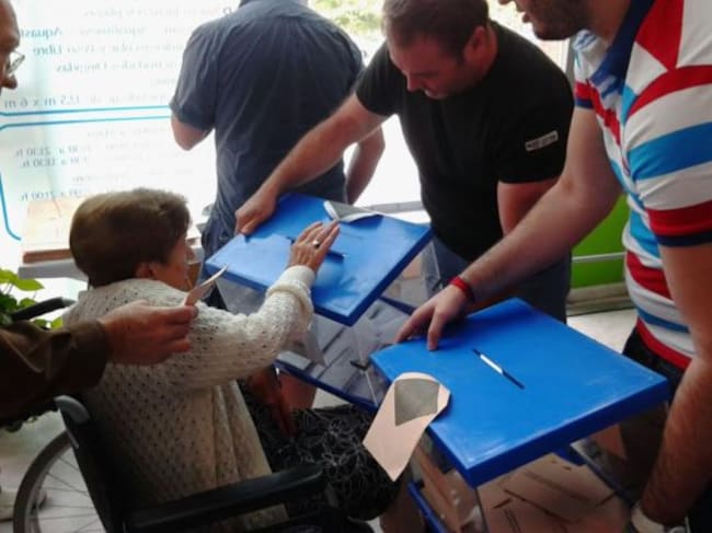 Los componentes de una mesa electoral acercan las urnas a una mujer en silla de ruedas.