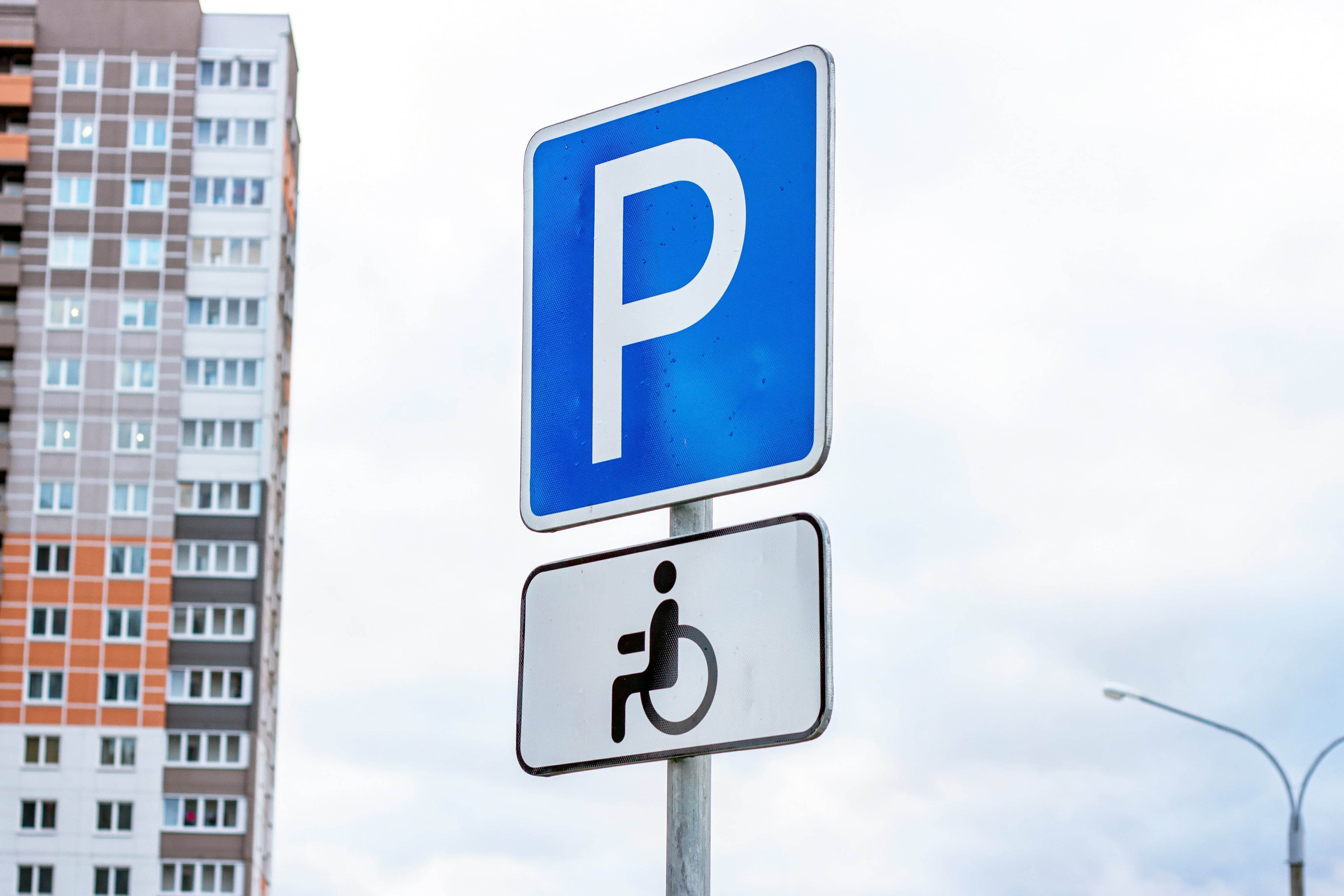 Blue and white parking sign with wheelchair for people with disabilities against sky and city buildings background.