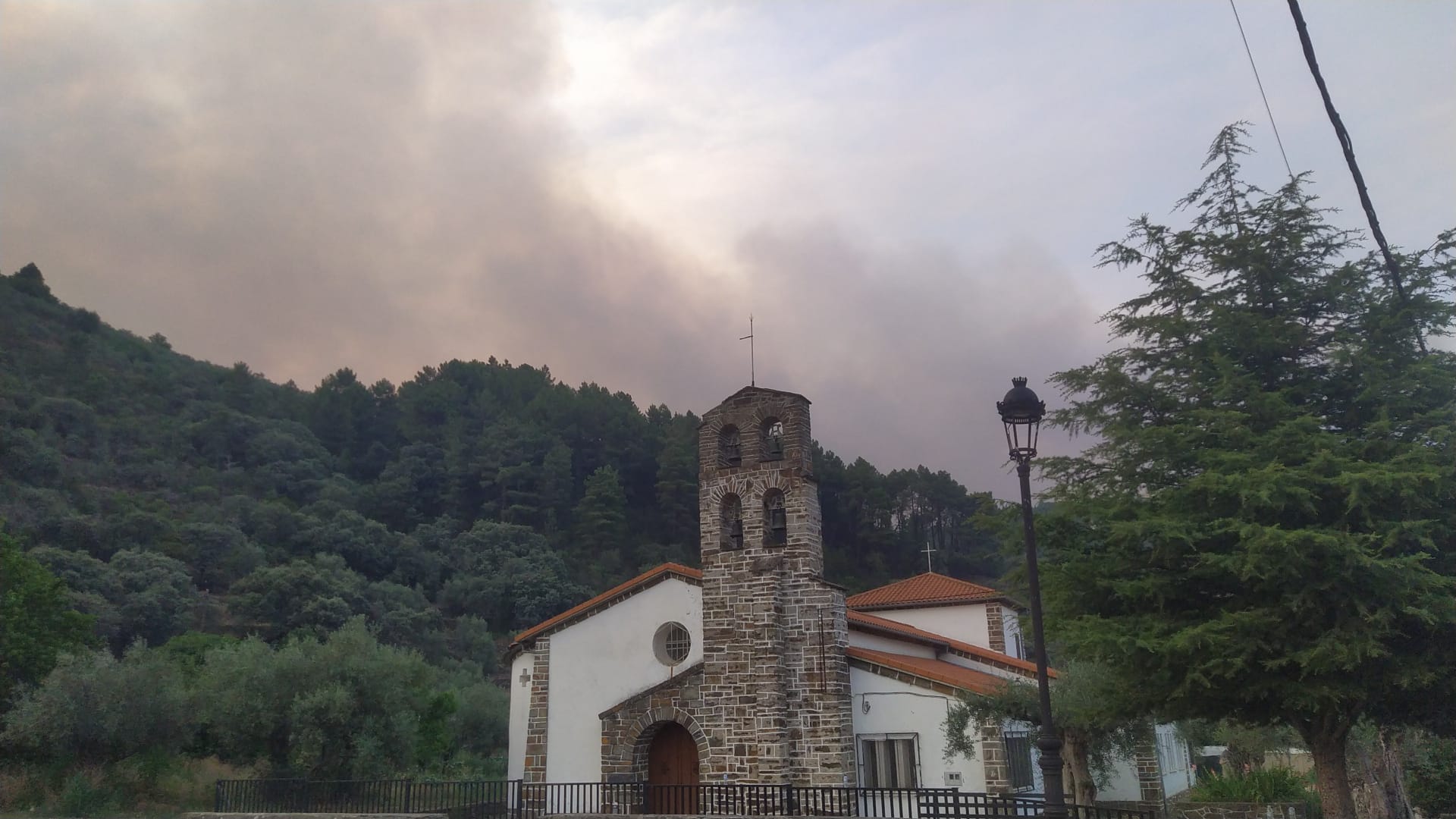 La iglesia de Nuñomoral con la densa columna de humo del incendio originado en el Cabezo a su espalda