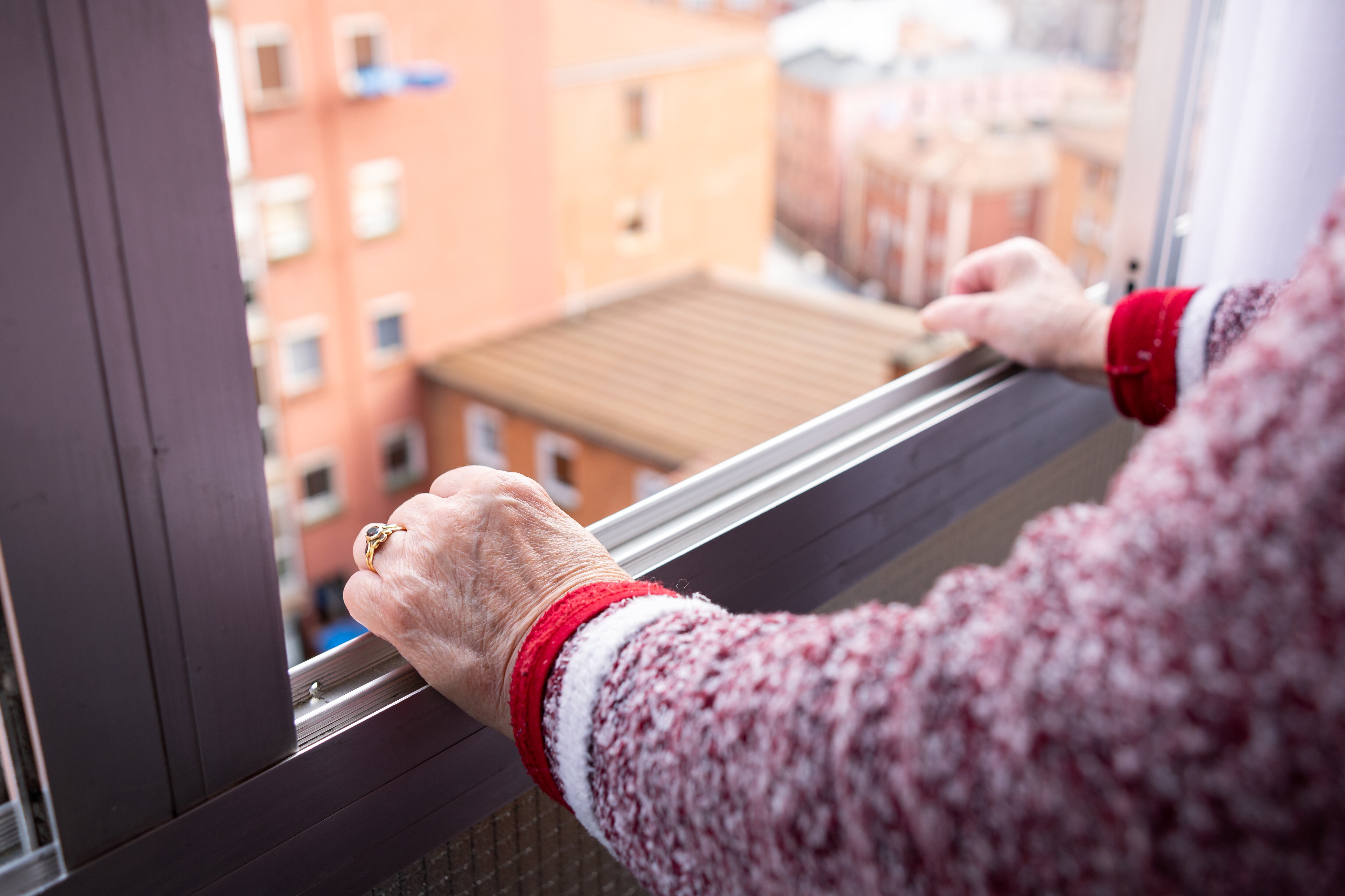 a old woman leaning out the window of a high floor in the city in solitude