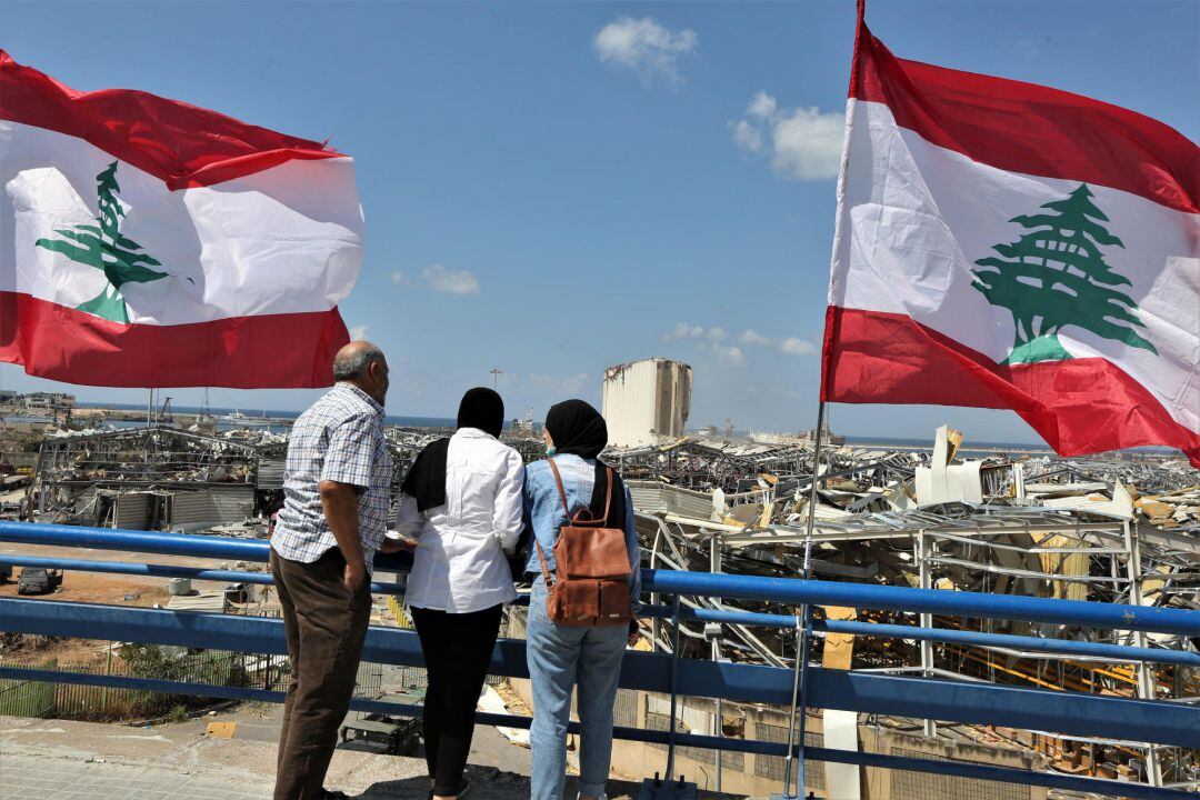 Gente con banderas del Líbano observan la destrucción causada por la explosión.