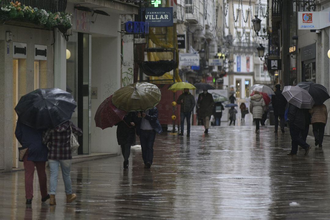 Transeúntes caminan protegidos por una vía de A Coruña, Galicia, a 20 de enero de 2021.