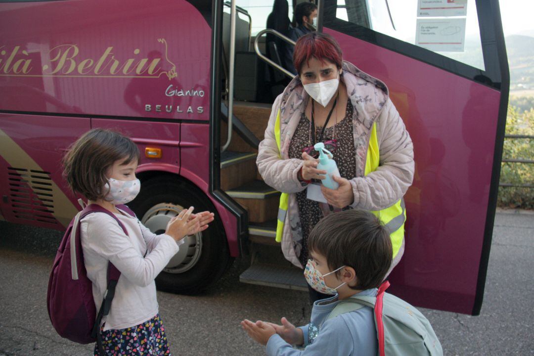 Una monitora de transporte escolar proporciona gel hidroalhólico a dos alumnos