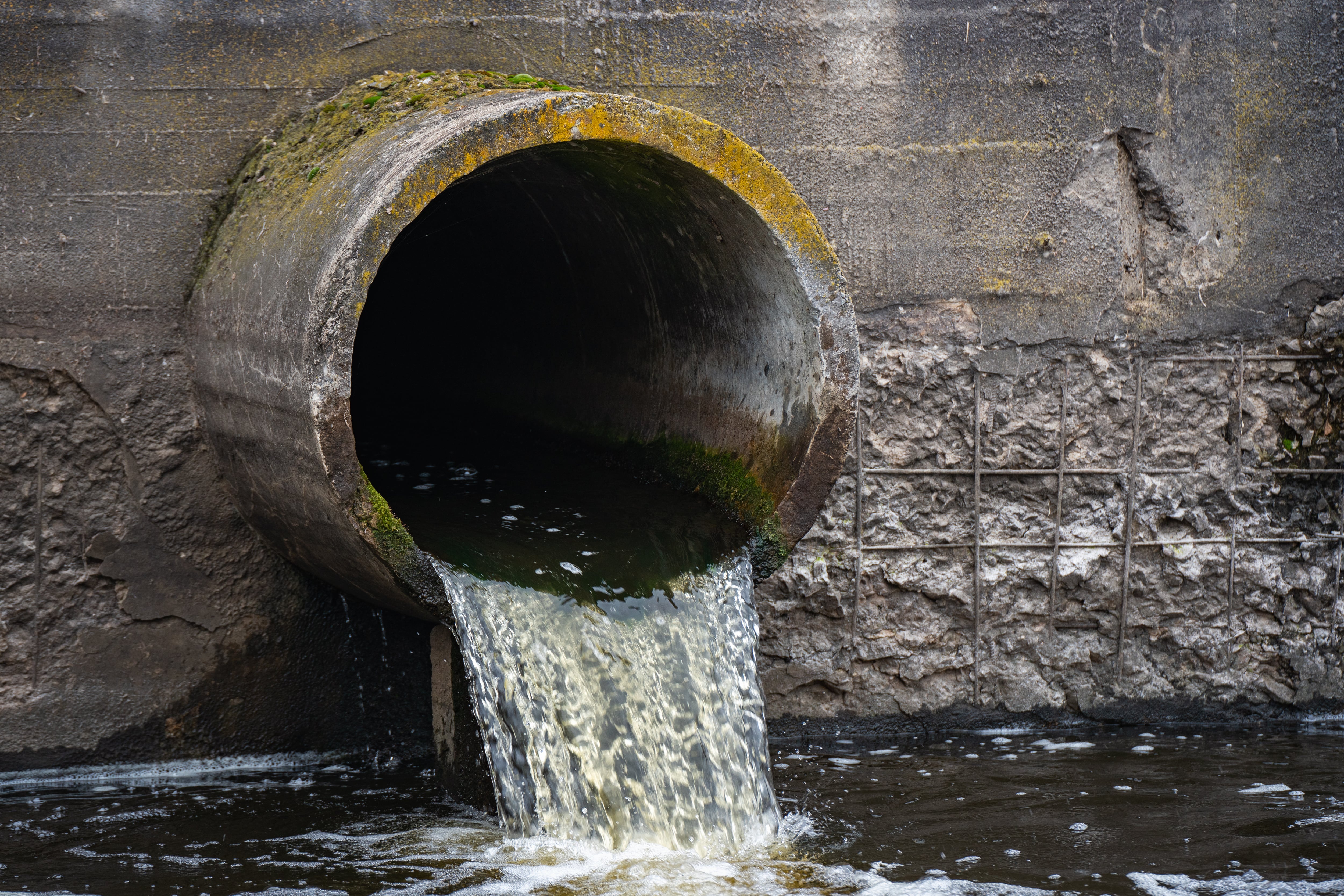 Dirty water flows from the pipe into the river, environmental pollution. Sewerage, treatment facilities.