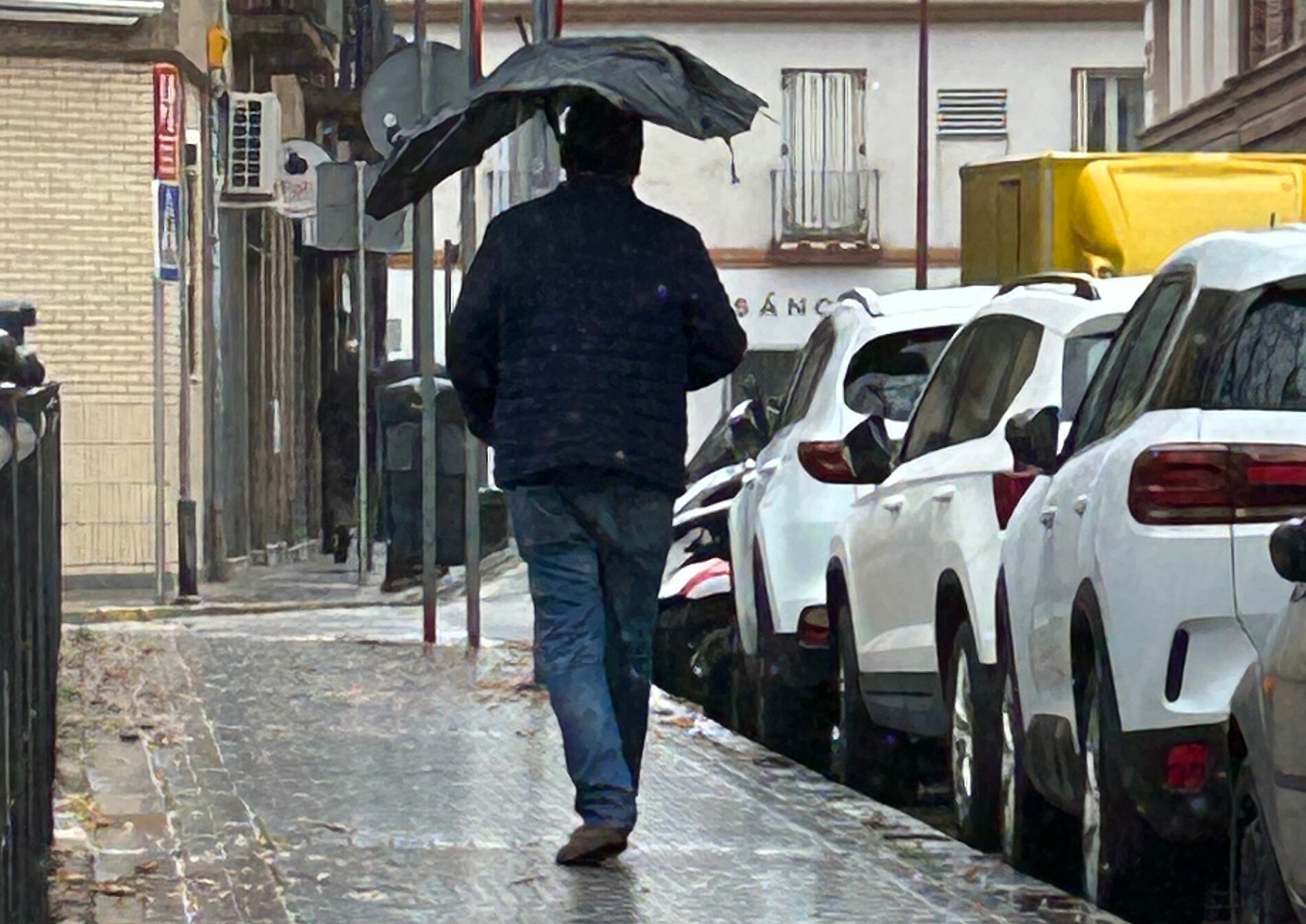 Un hombre camina con el paraguas casi destrozado por una calle de Sevilla.