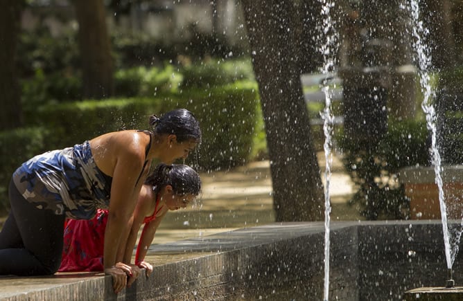 Dos jóvenes se refrescan en una fuente en Sevilla en un día de fuerte calor