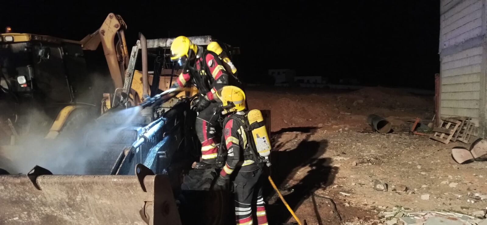 Los bomberos junto a la pala mecánica incendiada.