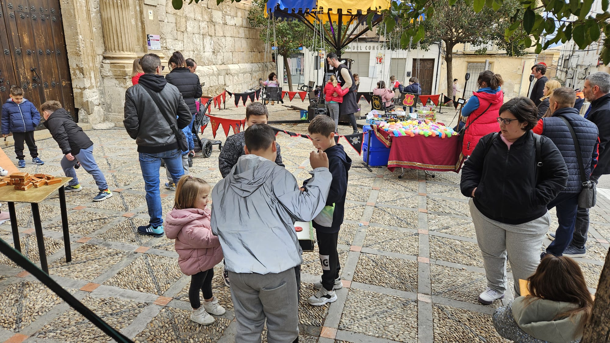 Niños y niñas juegan con juegos tradicionales, instalados en la Lonja de la Iglesia de la Asunción de Nuestra Señora