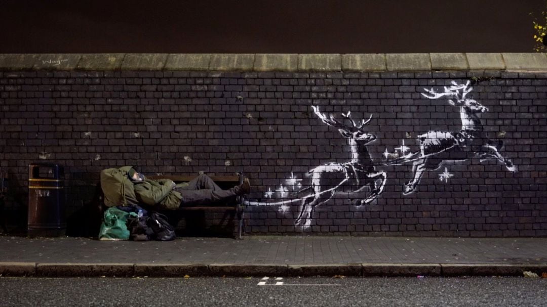 Un hombre duerme junto a un mural de Banksy