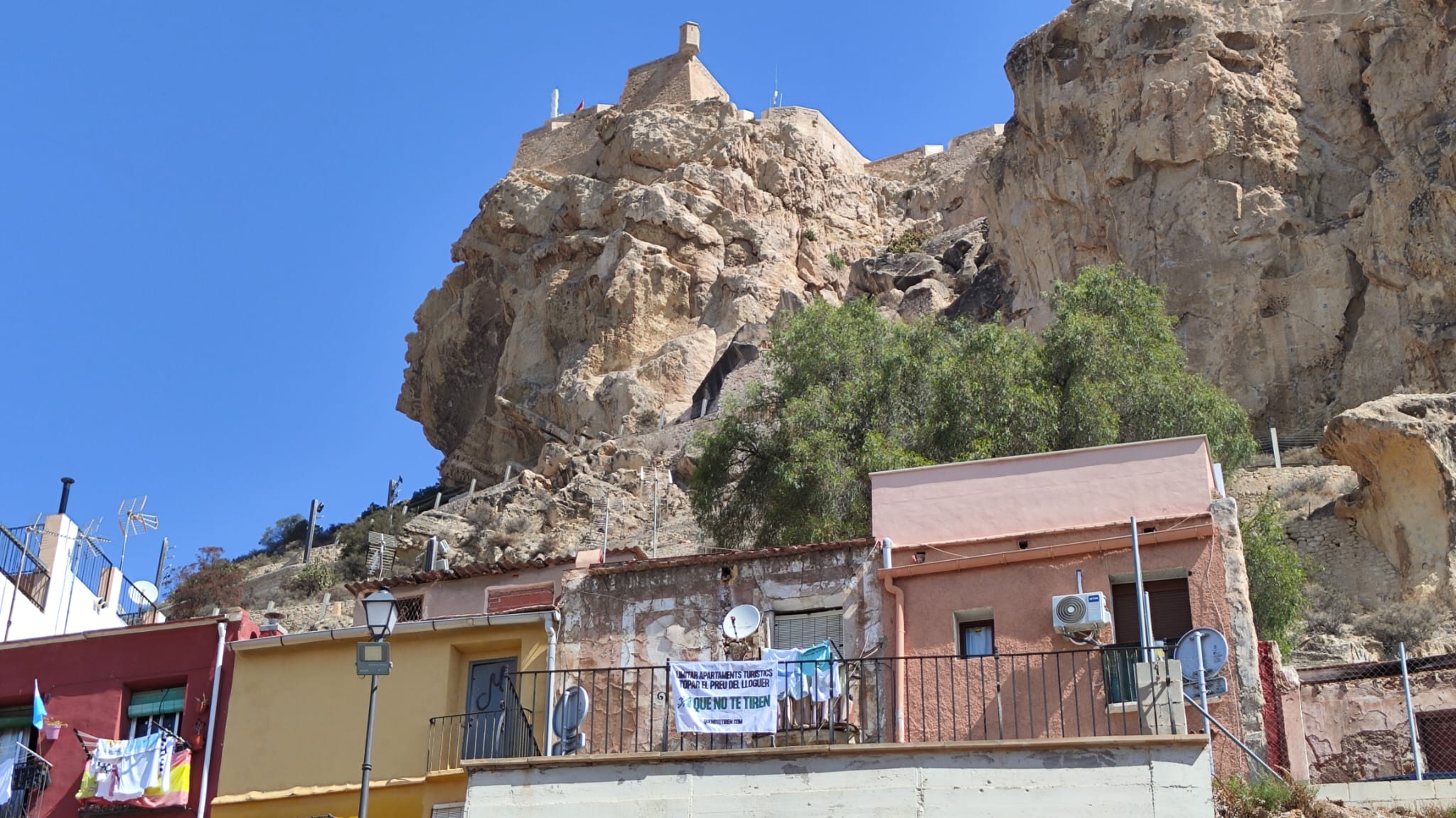 Casas a los pies de la Cara del Moro en el monte Benacantil de Alicante y un cartel contra los pisos turísticos ilegales