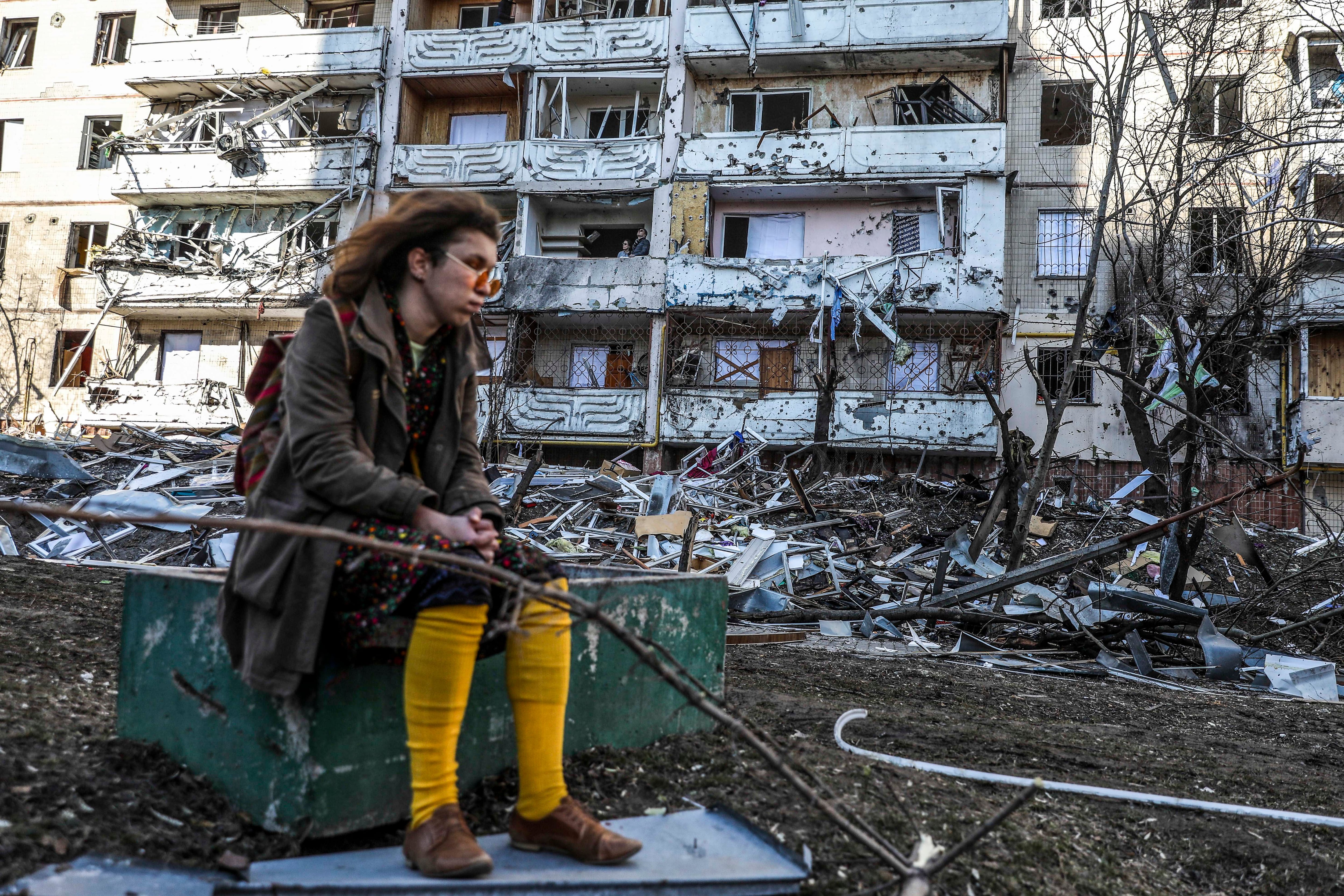 Una mujer sentada frente a un edificio derruido en Kiev