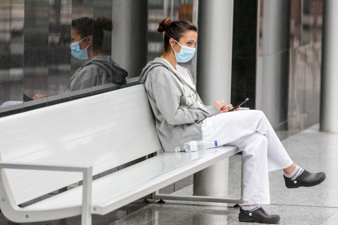 Una mujer sentada en un banco protegida con una mascarilla.