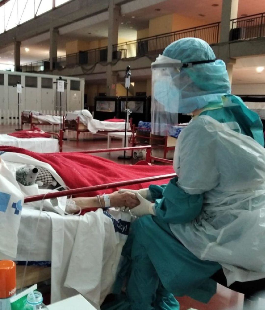 La imagen de una enfermera tomando la mano de una paciente en el hospital de campaña resume el trabajo del personal sanitario contra la pandemia y la soledad de los pacientes