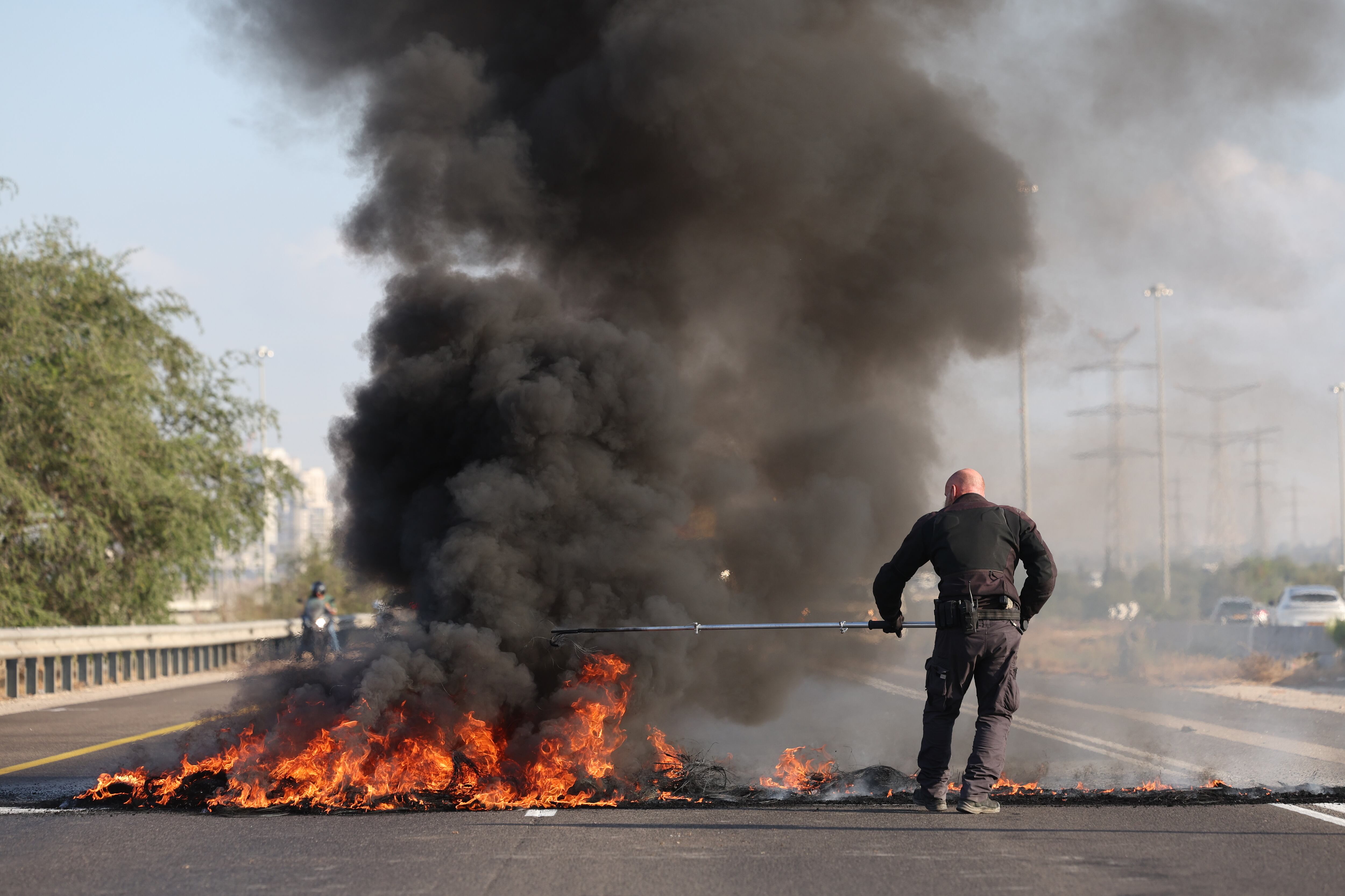 Un agente de policía israelí trabaja para extinguir los neumáticos en llamas que han prendido fuego los manifestantes en la carretera principal que conecta Tel Aviv y Jerusalén, Israel, el 17 de agosto de 2025.