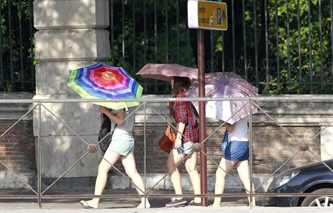 Varias jóvenes se protegen del sol con sus paraguas, en el Paseo del Rey de Madrid, para intentar mitigar las altas temperaturas que se registran en la capital