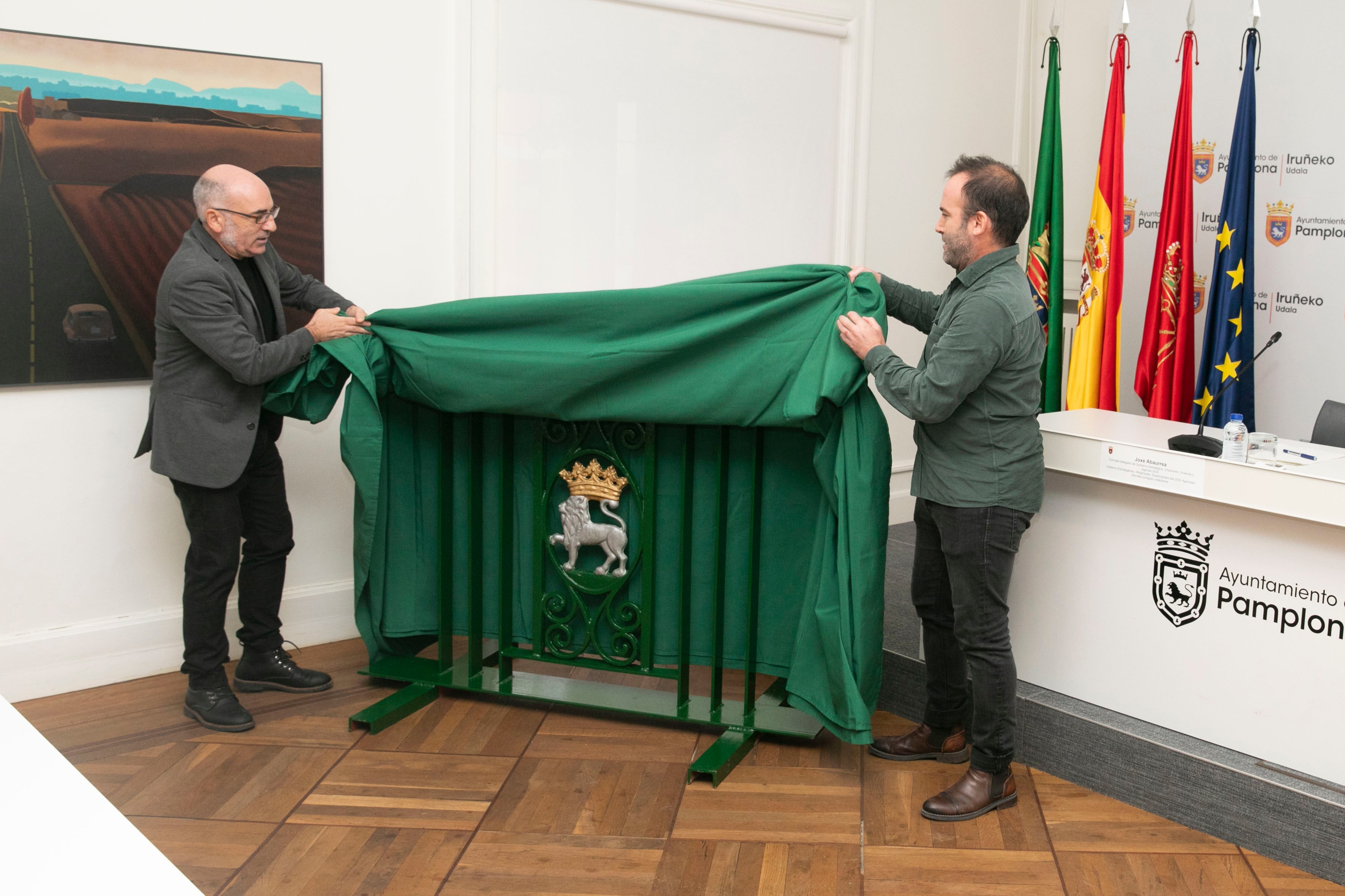 Los concejales Abaurrea e Izaguirre junto a una valla con uno de los escudos recuperados