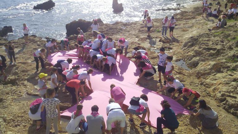 Grupo de voluntarias colocando el gran lazo rosa en la playa de Les Arenetes, de Dénia, con motivo del Día Mundial contra el Cáncer de Mama.