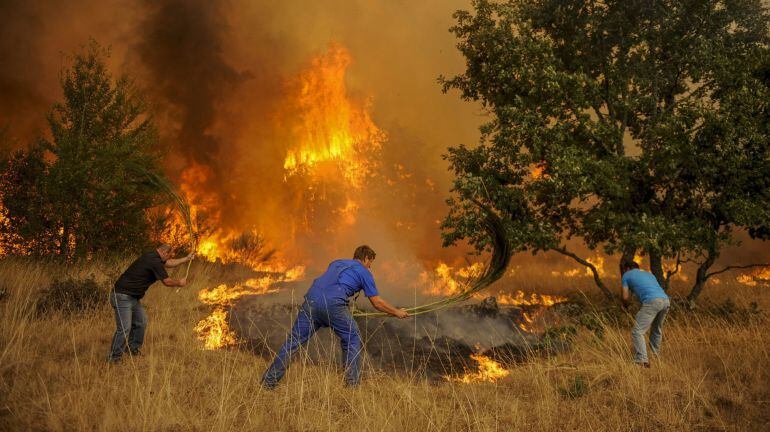 Vecinos de la localidad realizan labores de extinción para intentar controlar el incendio forestal próximo a las casas, registrado en Cualedro, en el sur de la provincia de Ourense