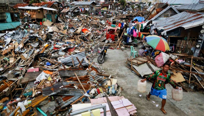 Un sobreviviente lleva latas de agua en su búsqueda de agua dulce en una zona devastada por el tifón Yolanda en Tacloban